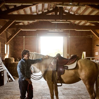 Uomo che sella un cavallo in una scuderia di legno